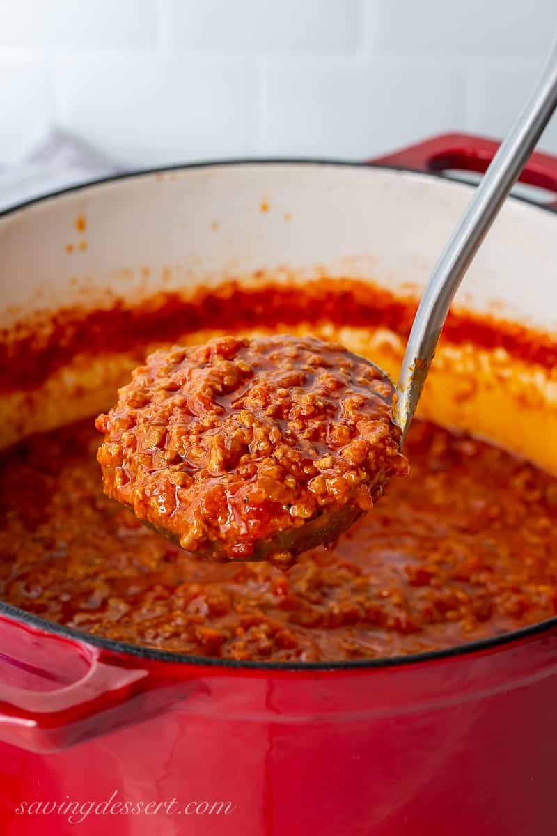 A ladle of bolognese sauce over a Dutch oven