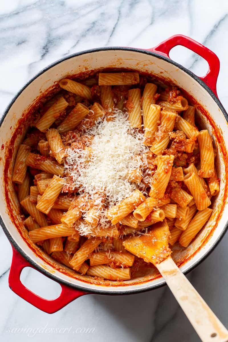 An overhead view of a pot of rigatoni bolognese sauce topped with shredded Parmesan