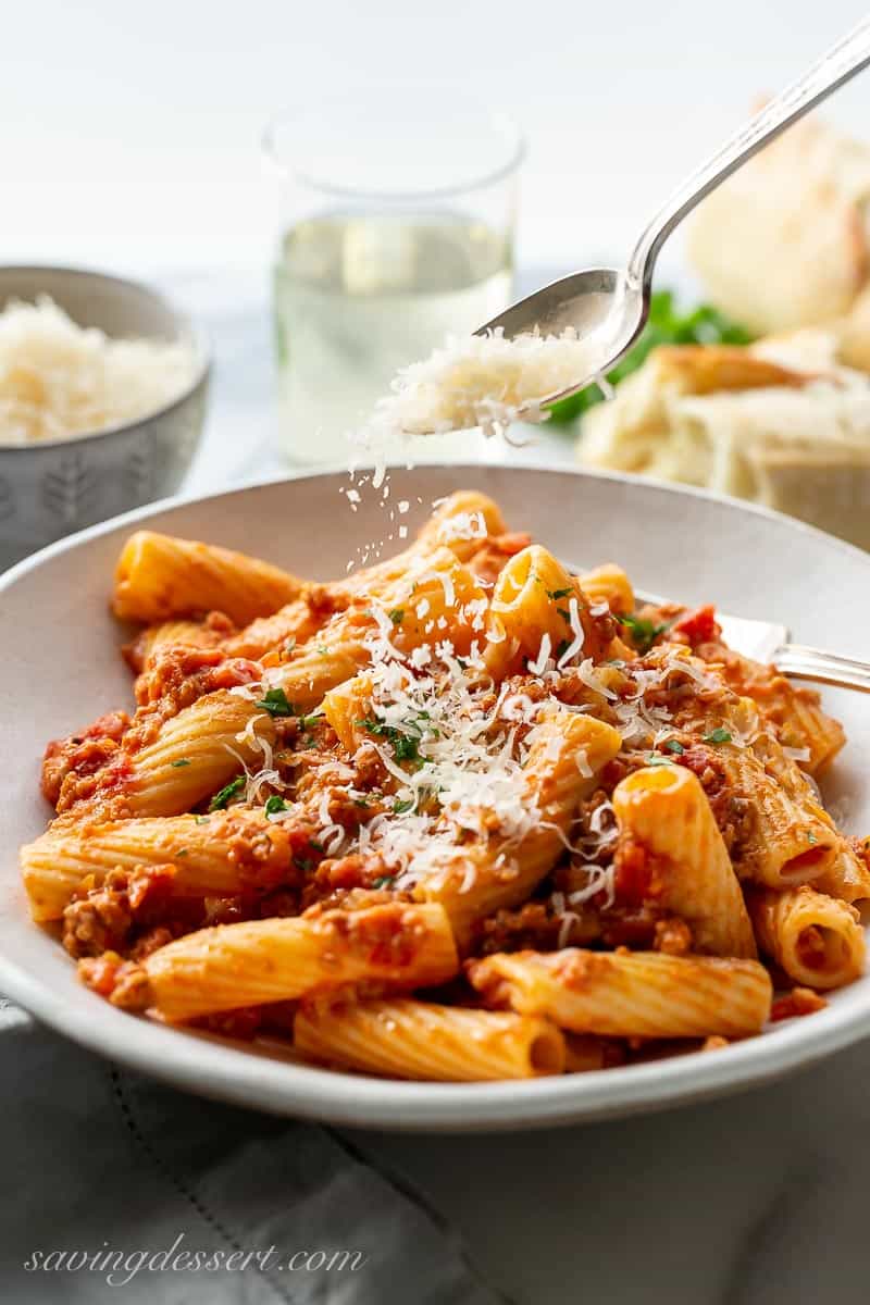 A bowl of bolognese being sprinkled with fresh grated Parmesan cheese