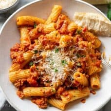 Overhead view of a bowl of rigatoni bolognese garnished with parsley and fresh grated Parmesan