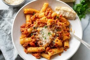 Overhead view of a bowl of rigatoni bolognese garnished with parsley and fresh grated Parmesan