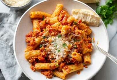 Overhead view of a bowl of rigatoni bolognese garnished with parsley and fresh grated Parmesan
