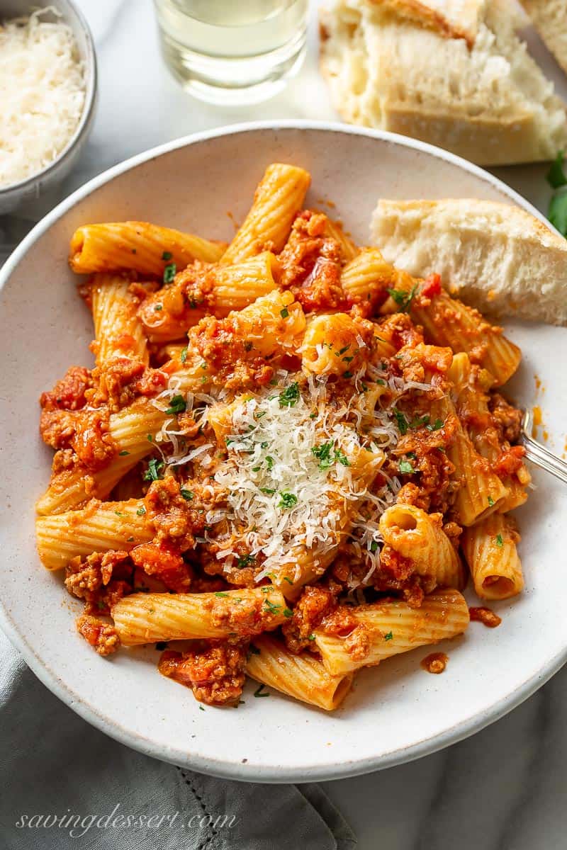 Overhead view of a bowl of rigatoni with bolognese sauce and a hunk of crusty bread