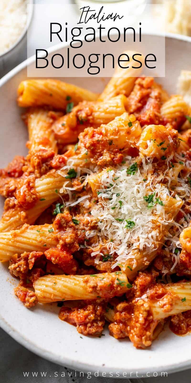 An overhead view of a bowl of Rigatoni Bolognese garnished with fresh grated Parmesan