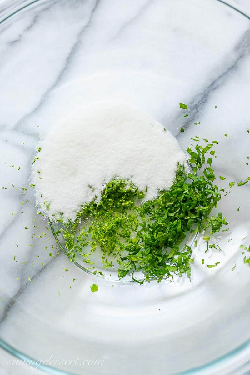 A large mixing bowl with sugar, mint leaves and lime zest