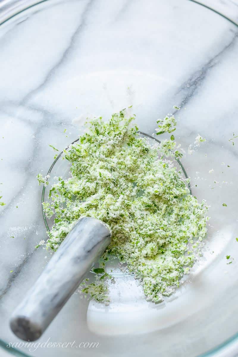 A bowl with muddled lime zest, sugar and minced mint leaves