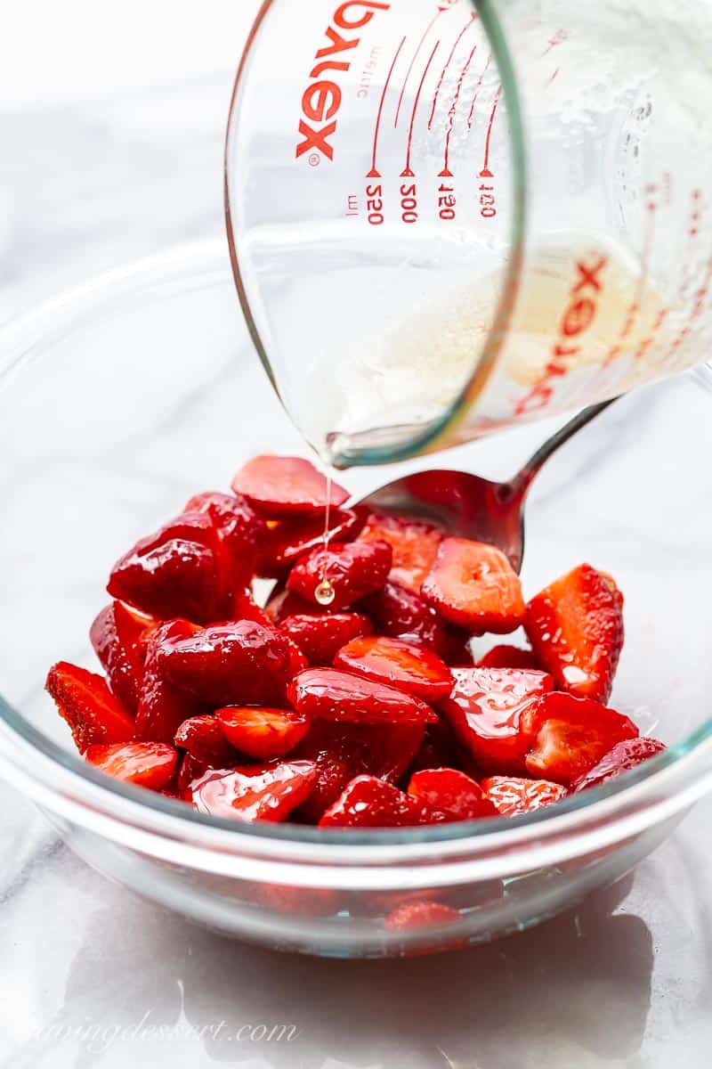 A bowl of fresh strawberries being drizzled with a simple syrup
