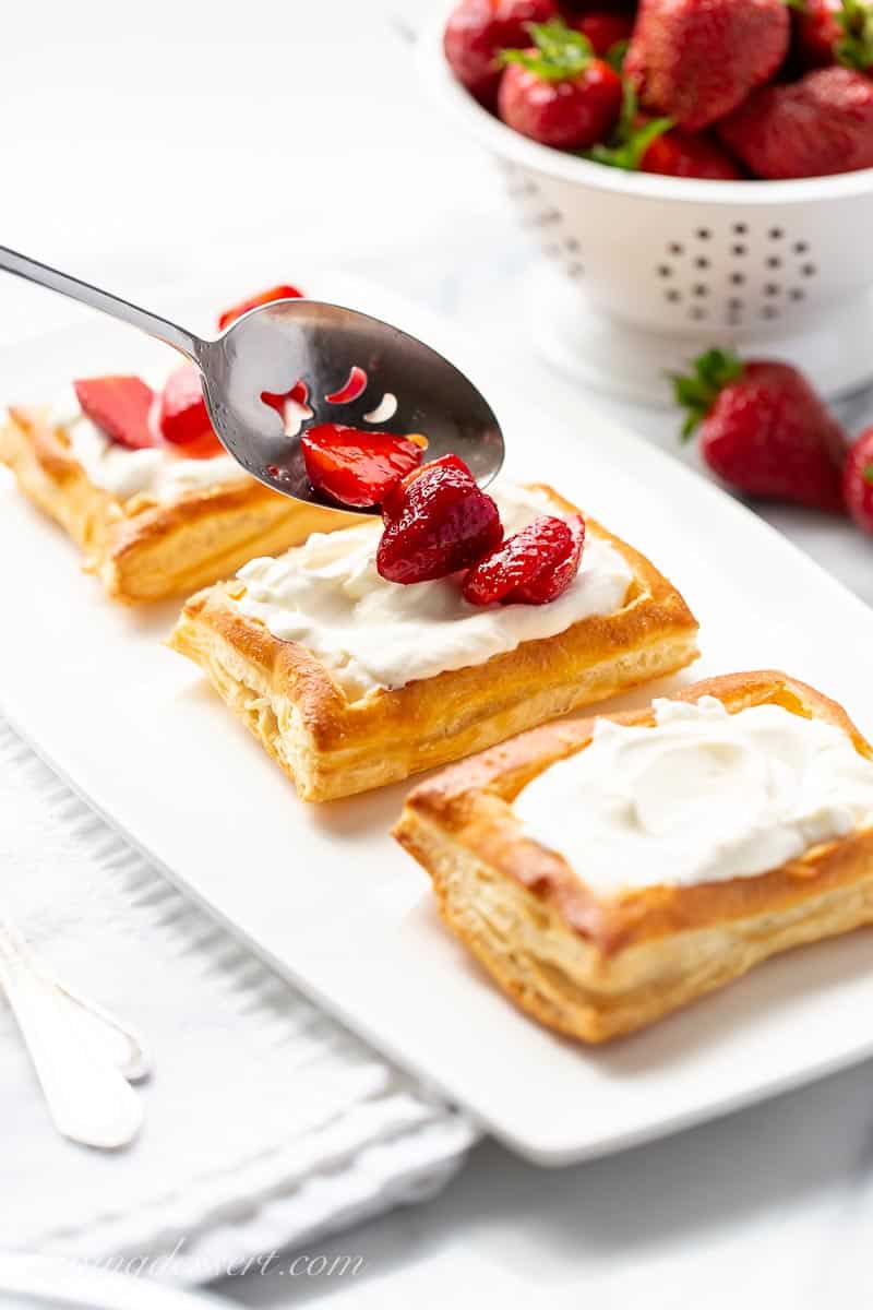Strawberries being spooned into puff pastry shells filled with cream