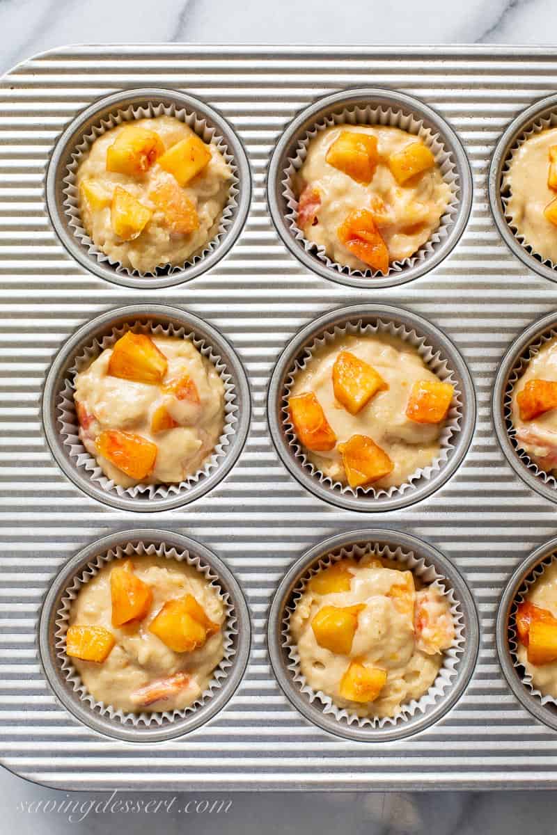 a muffin tin with peach batter in each well