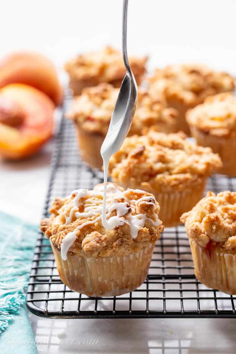 A peach crumble muffin on a cooling rack being drizzled with icing
