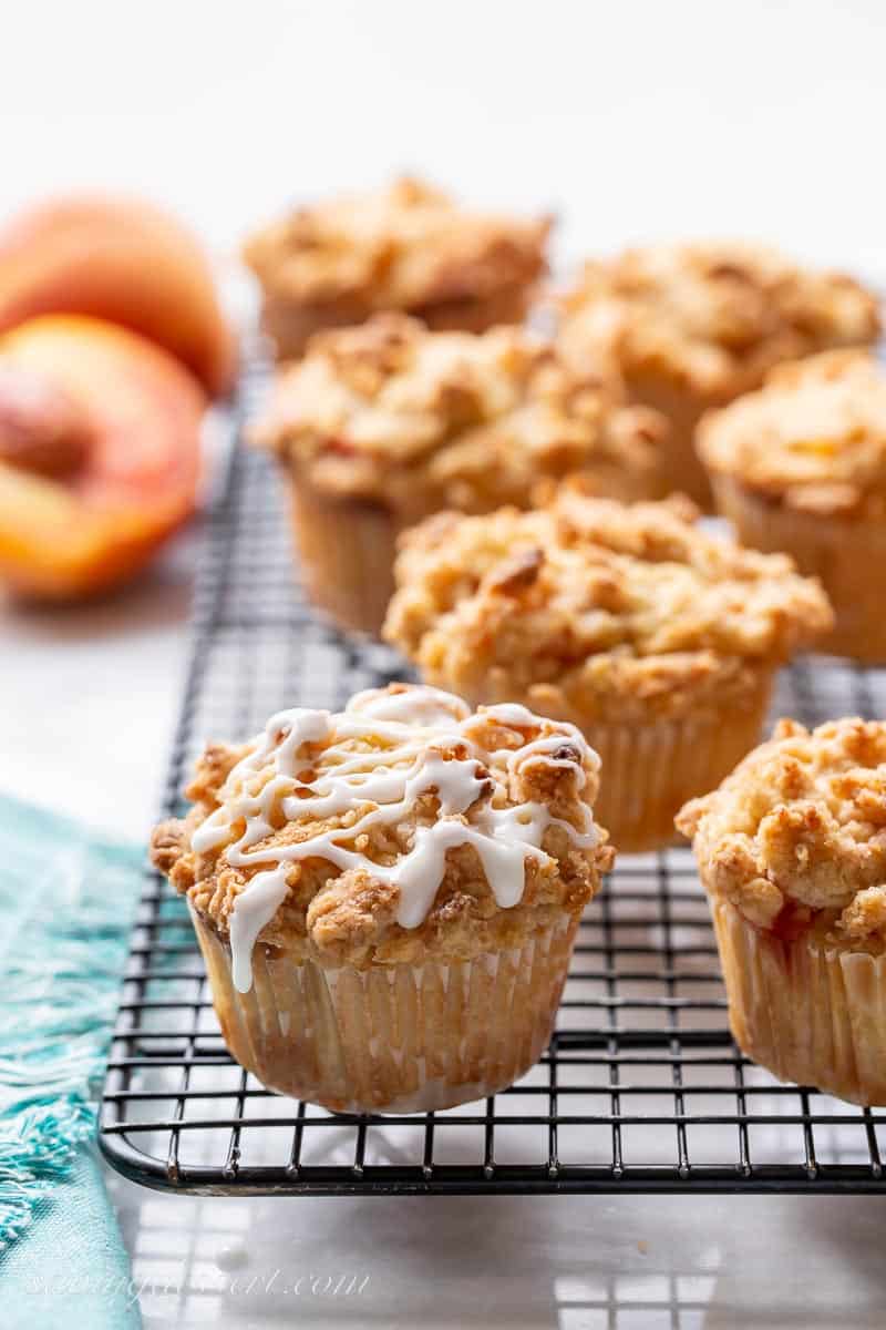 Baked peach crumble muffins on a cooling rack one with drizzled icing