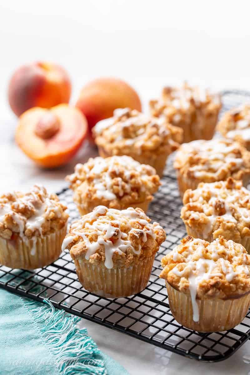 Peach muffins with a crumble topping and drizzled almond icing on a cooling rack