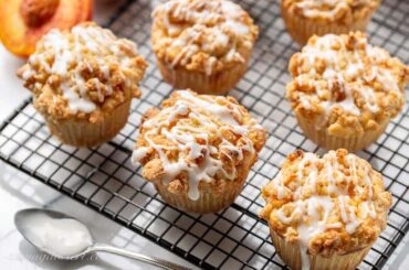 Peach crumble muffins topped with a drizzled icing on a cooling rack
