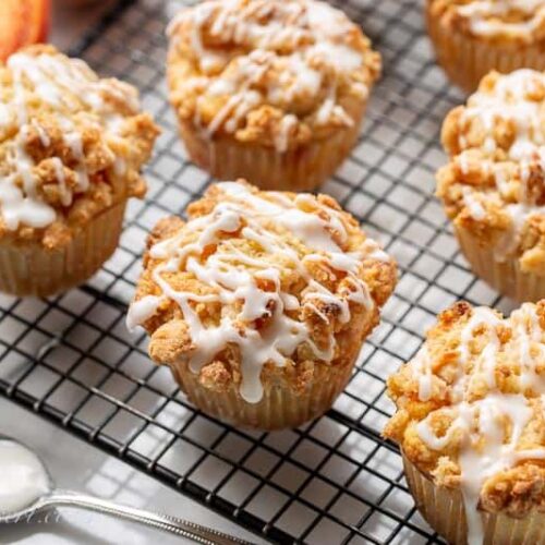 Peach crumble muffins topped with a drizzled icing on a cooling rack