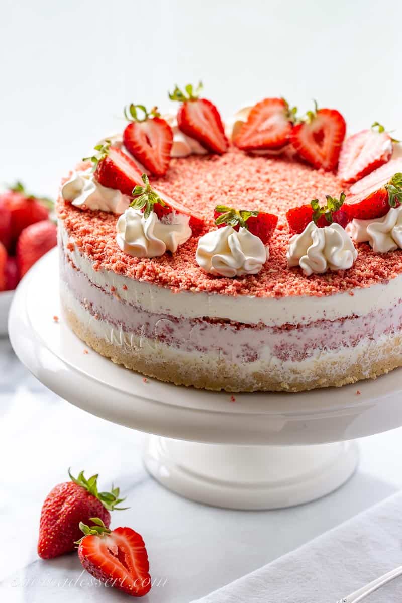 A layered Strawberry crunch cake on a cake stand with fresh strawberries on top