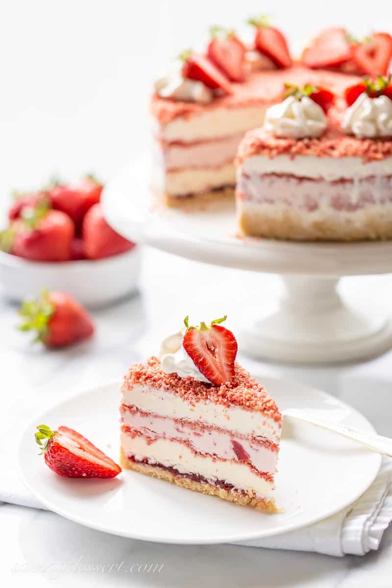 A slice of strawberry ice cream crunch cake on a plate with a fresh strawberry garnish