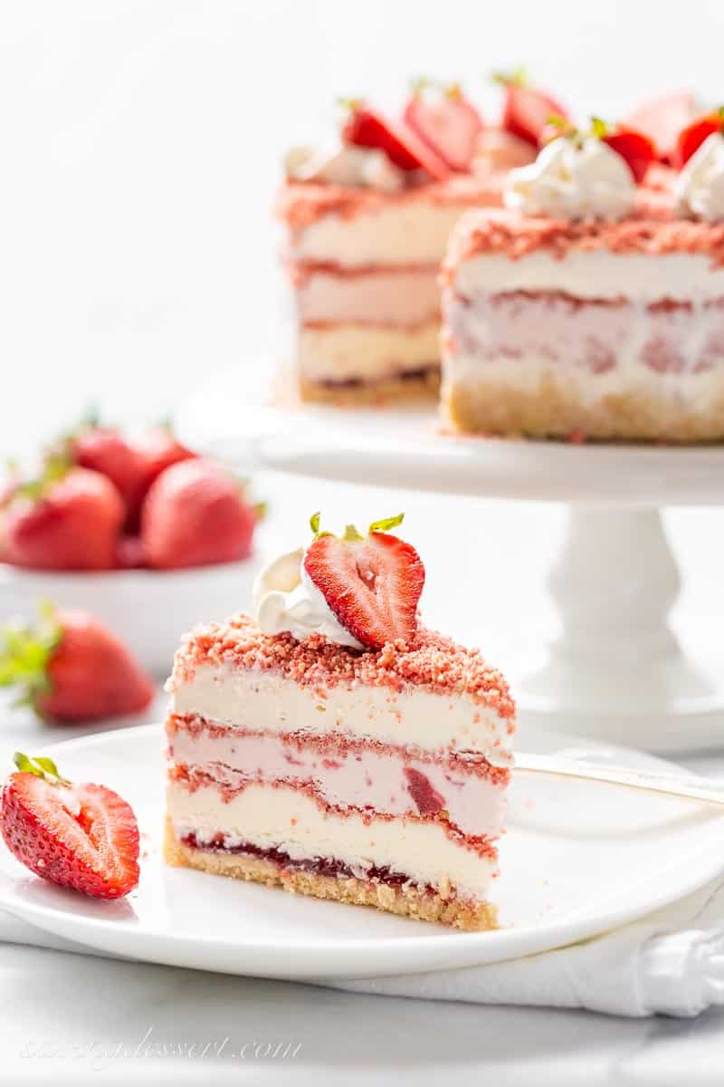 A slice of strawberry ice cream crunch cake on a plate with a fresh strawberry garnish