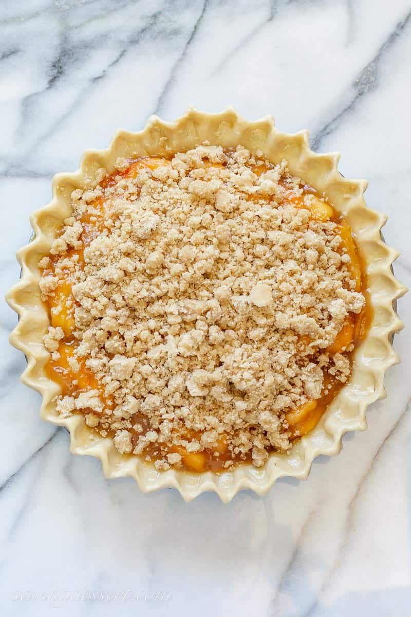An unbaked peach pie with a crumble topping