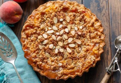 Peach Crumble Pie on a table with an ice cream scoop and pie spatula