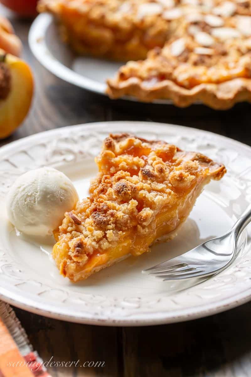 A slice of peach crumble pie on a plate with a scoop of vanilla ice cream