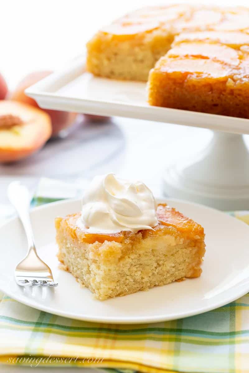 A piece of peach cake on a plate with a fork and whipped cream