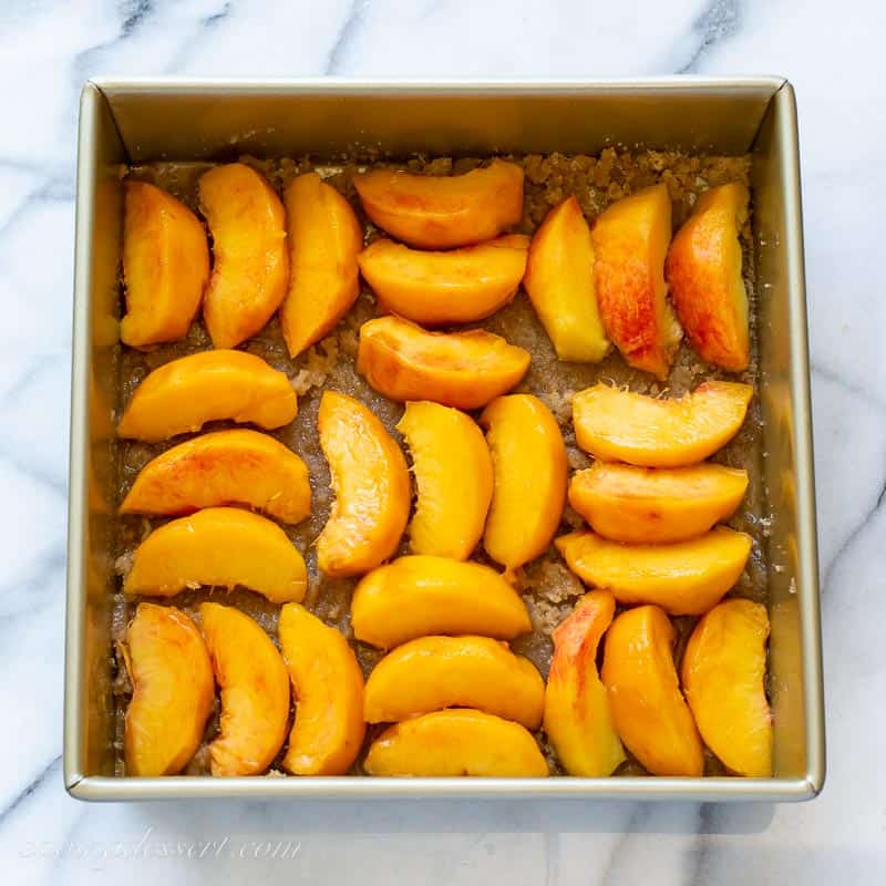 sliced peaches in a square cake pan on top of a brown sugar butter mixture