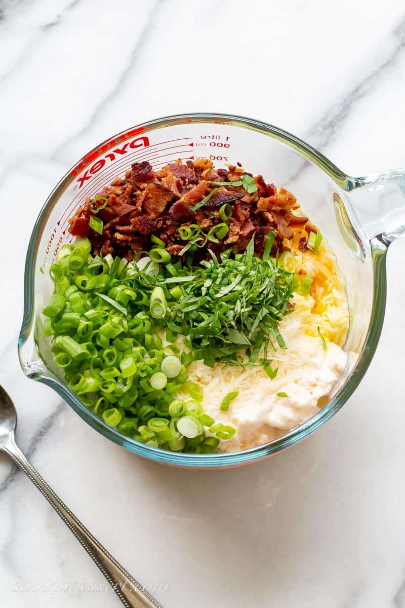 a large measuring cup filled with mayo, scallions, cheese, basil and bacon