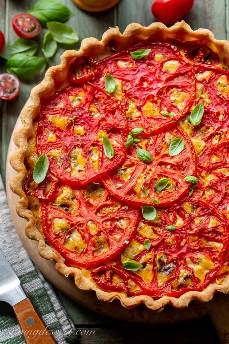 Closeup overhead view of a golden brown crust on a tomato pie garnished with basil leaves