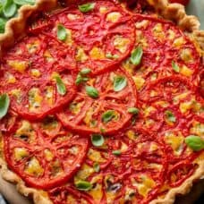 A closeup of a tomato pie topped with basil leaves