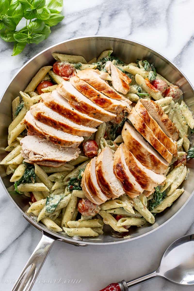 Overhead view of a skillet with sliced chicken breasts over pesto pasta