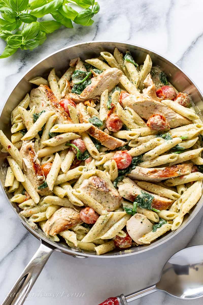 Overhead of a skillet filled with chicken pesto pasta with tomatoes and basil leaves