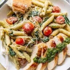 Overhead view of a bowl of penne pasta with sliced chicken, fresh basil pesto sauce and blistered tomatoes