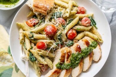 Overhead view of a bowl of penne pasta with sliced chicken, fresh basil pesto sauce and blistered tomatoes