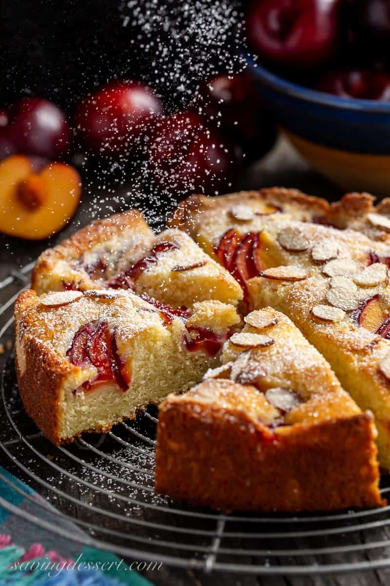 Sliced plum cake being dusted with powdered sugar
