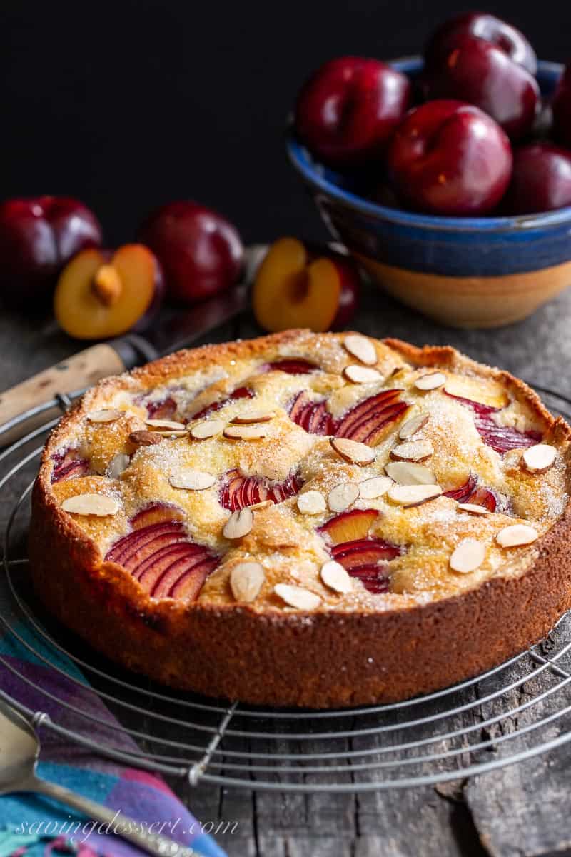 Side view of a simple rustic plum cake with a bowl of plums in the background