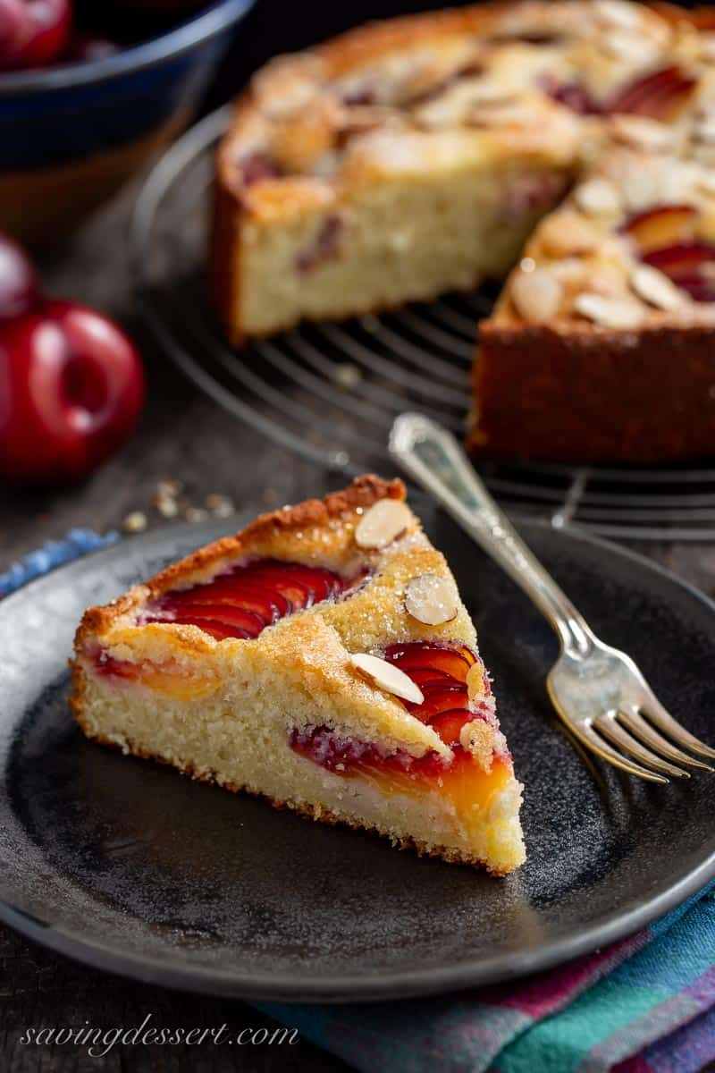 A slice of plum cake on a black plate with a fork