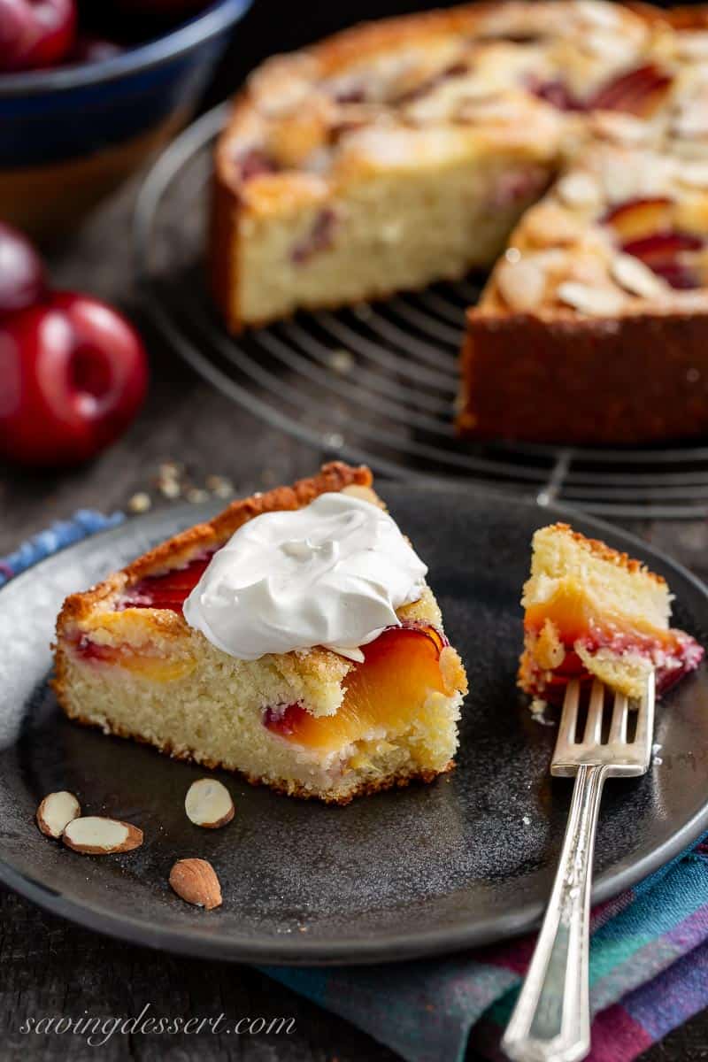 A slice of plum cake on a plate with a dollop of whipped cream on top