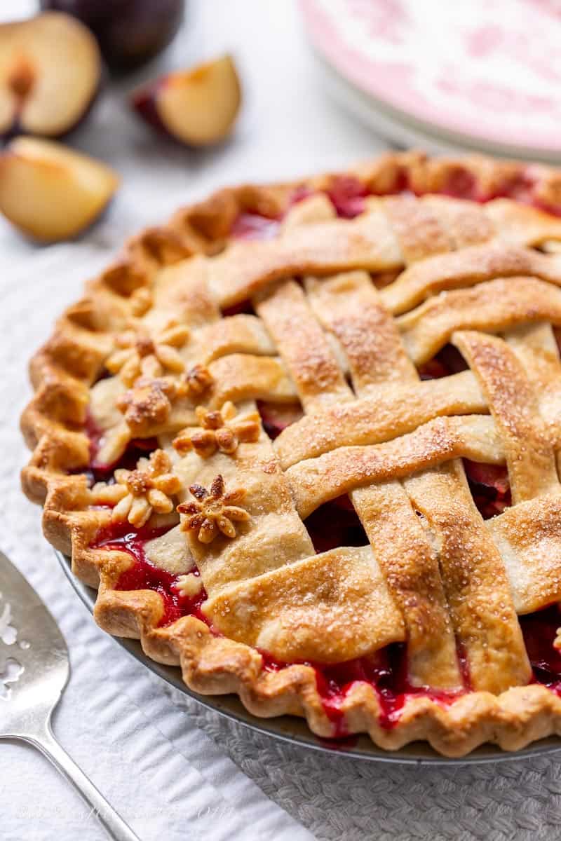 Side view of a golden brown baked plum pie with lattice top crust and tiny flower pastry cutouts