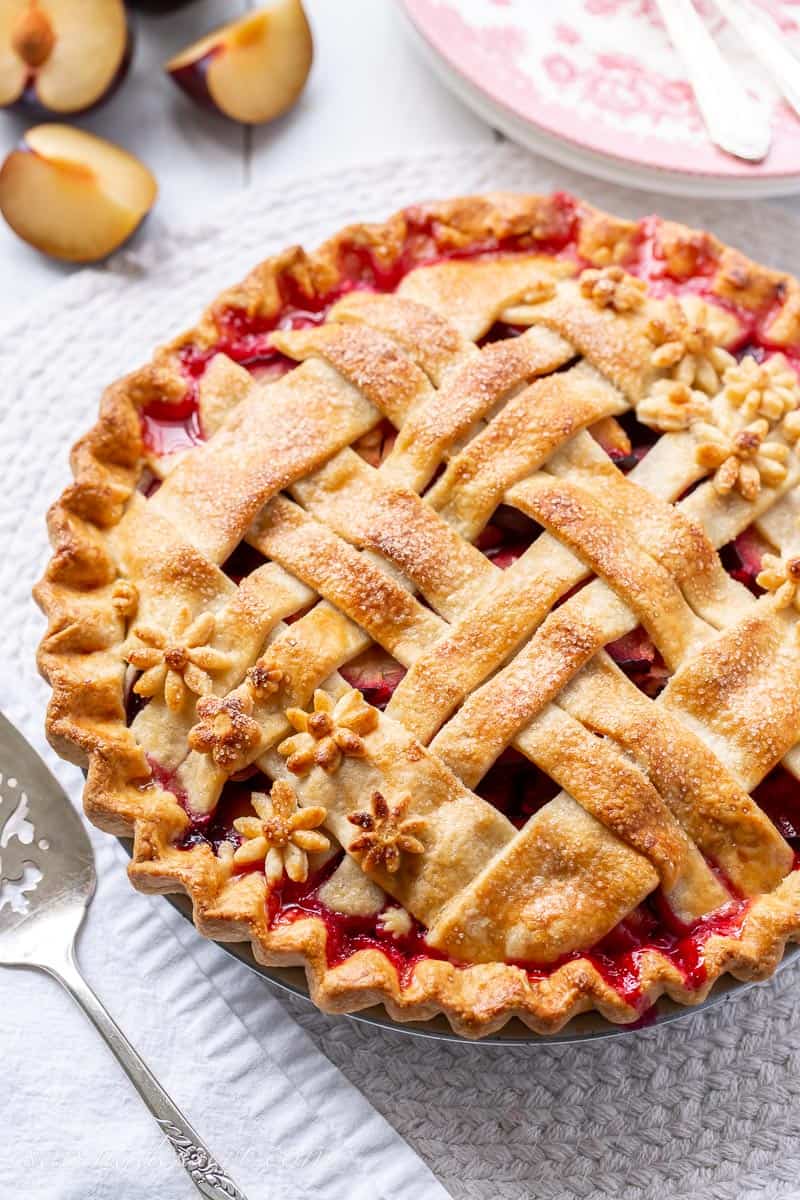 A golden brown baked plum pie with a lattice crust with juices bubbled up through the cracks