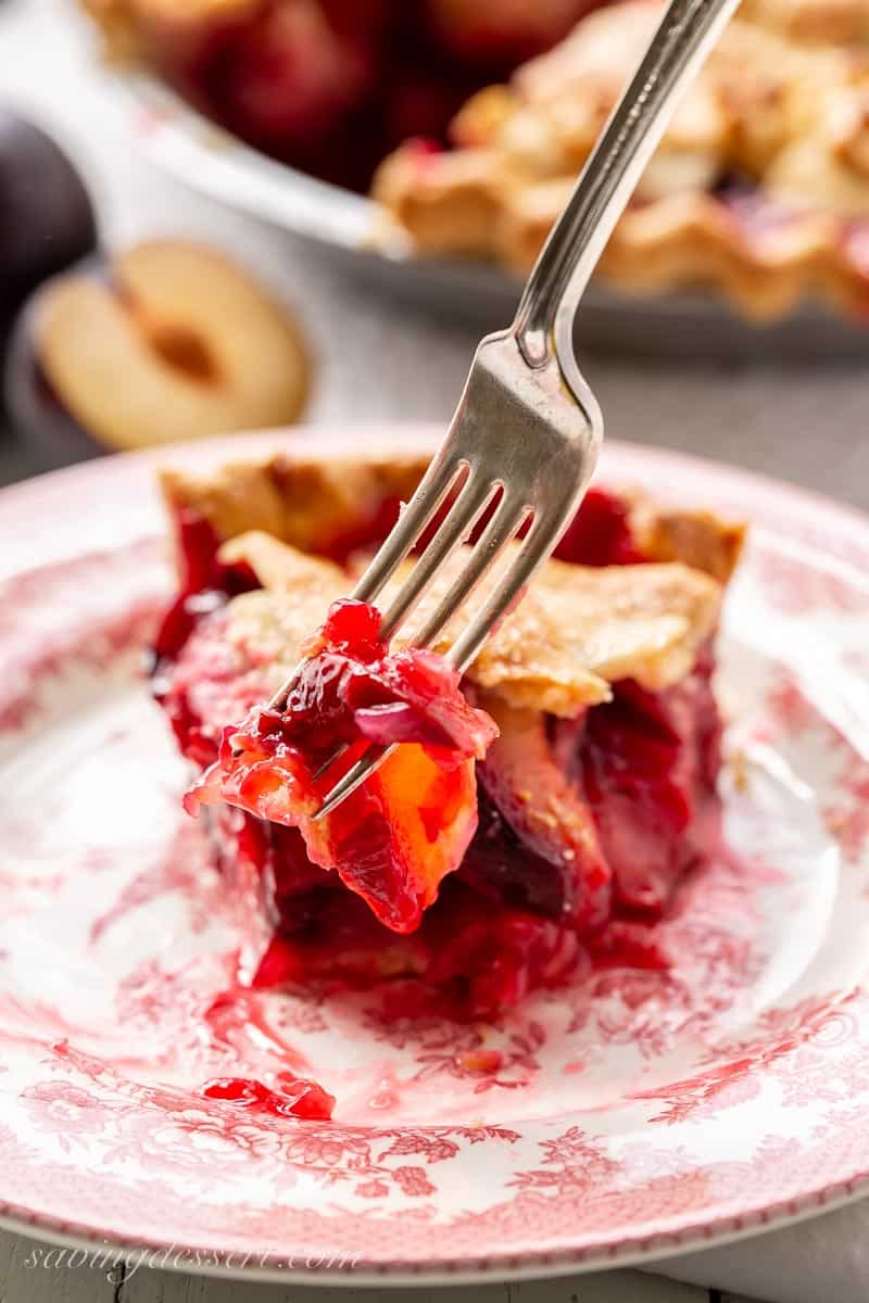 A slice of partially eaten plum pie on a plate with a fork