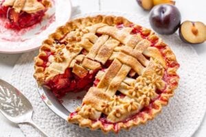 Plum pie with a slice taken out and fresh plums in the background