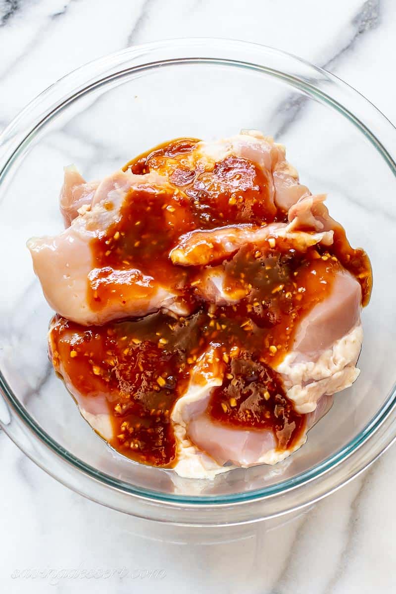A bowl of chicken thighs coated in a red sweet marinade
