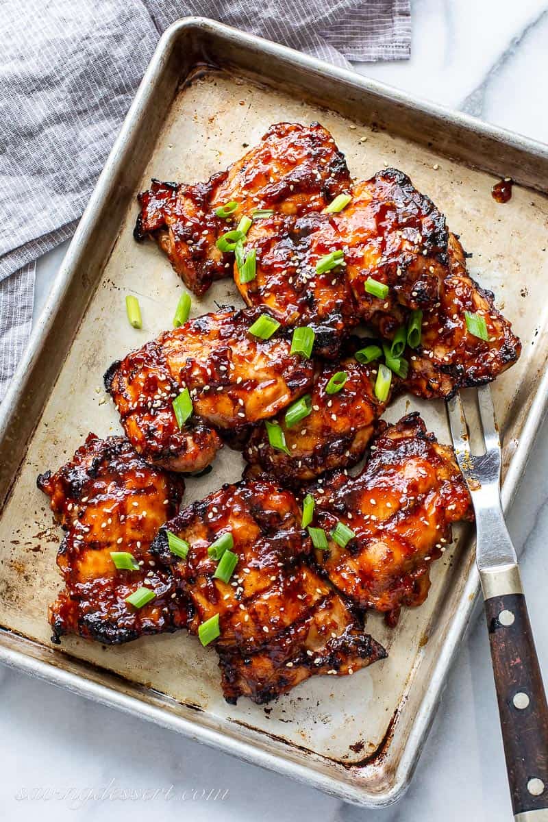 Grilled chicken thighs on a baking sheet garnished with sesame seeds and green onions