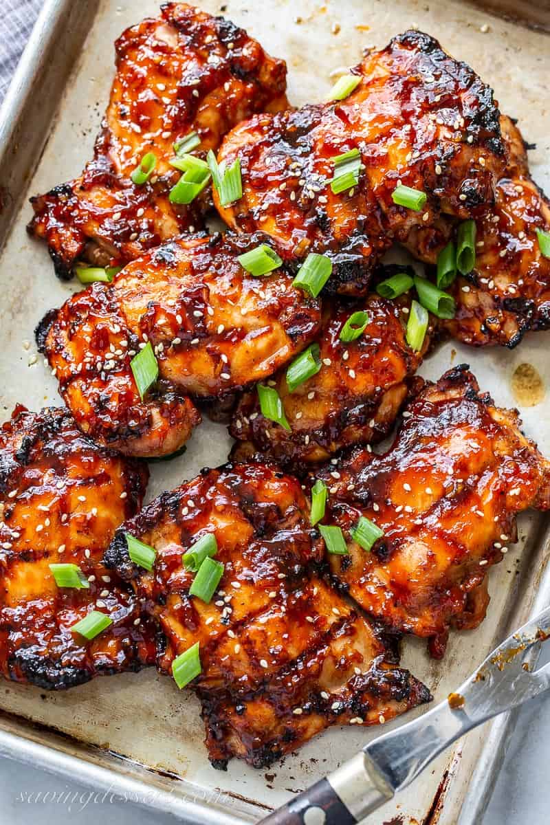Closeup of a baking tray filled with grilled Asian chicken thighs garnished with green onions and sesame seeds
