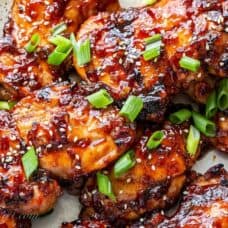 Closeup of grilled chicken thighs with a stick sweet Asian sauce, green onions and sesame seeds