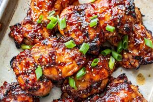 Closeup of grilled chicken thighs with a stick sweet Asian sauce, green onions and sesame seeds