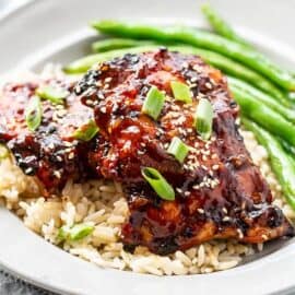 A dinner plate with grilled chicken thighs over brown rice with roasted green beans on the side
