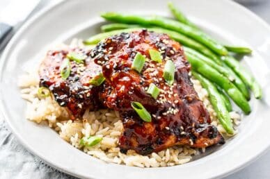 A dinner plate with grilled chicken thighs over brown rice with roasted green beans on the side