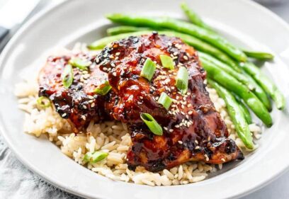 A dinner plate with grilled chicken thighs over brown rice with roasted green beans on the side