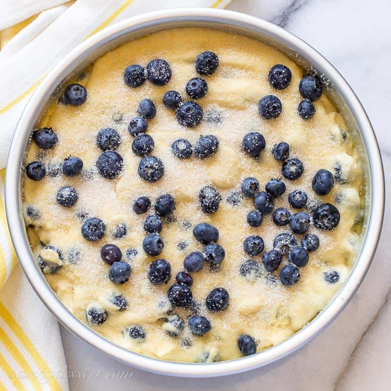 a cake pan filled with cornbread batter topped with coarse sugar and blueberries